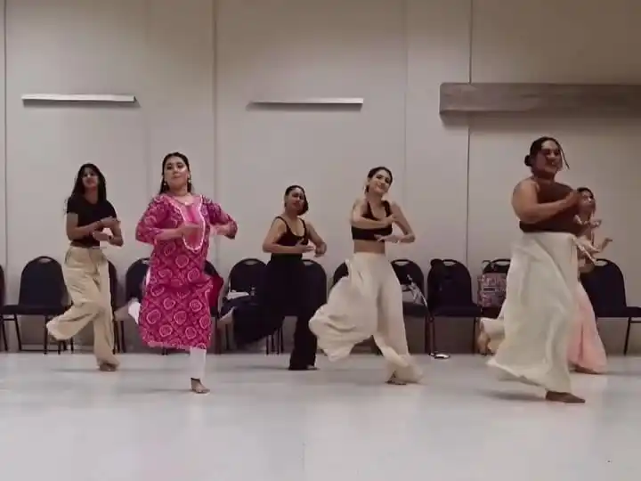 Dancer leading a group through a phrase in a wooden-floored rehearsal room