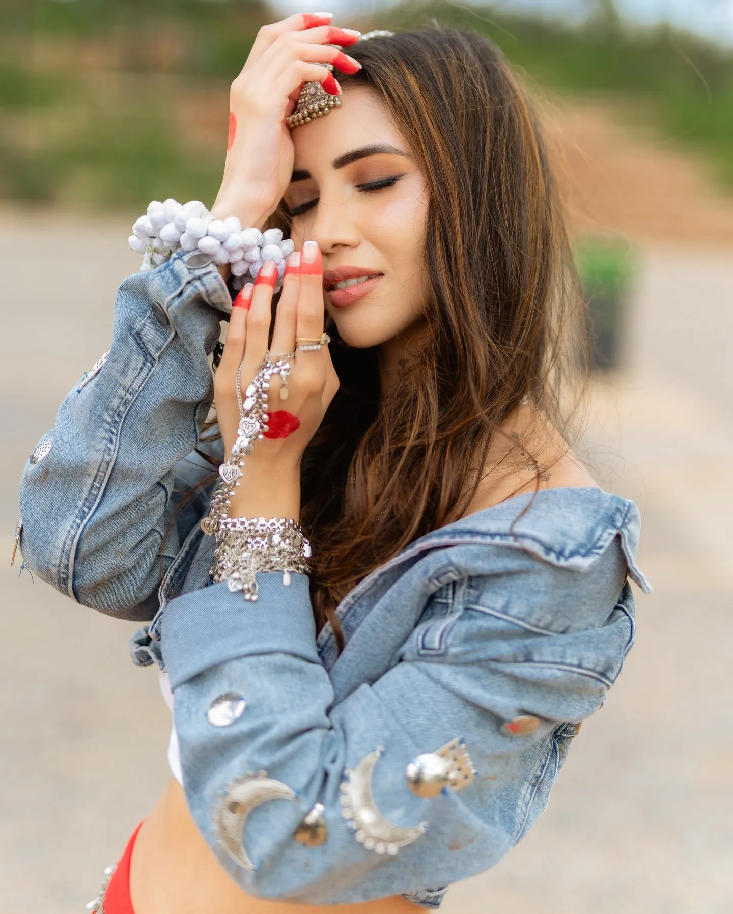Divaksha Jinabhai with her eyes closed and a hand raised to her forehead, in a denim jacket and silver jewellery