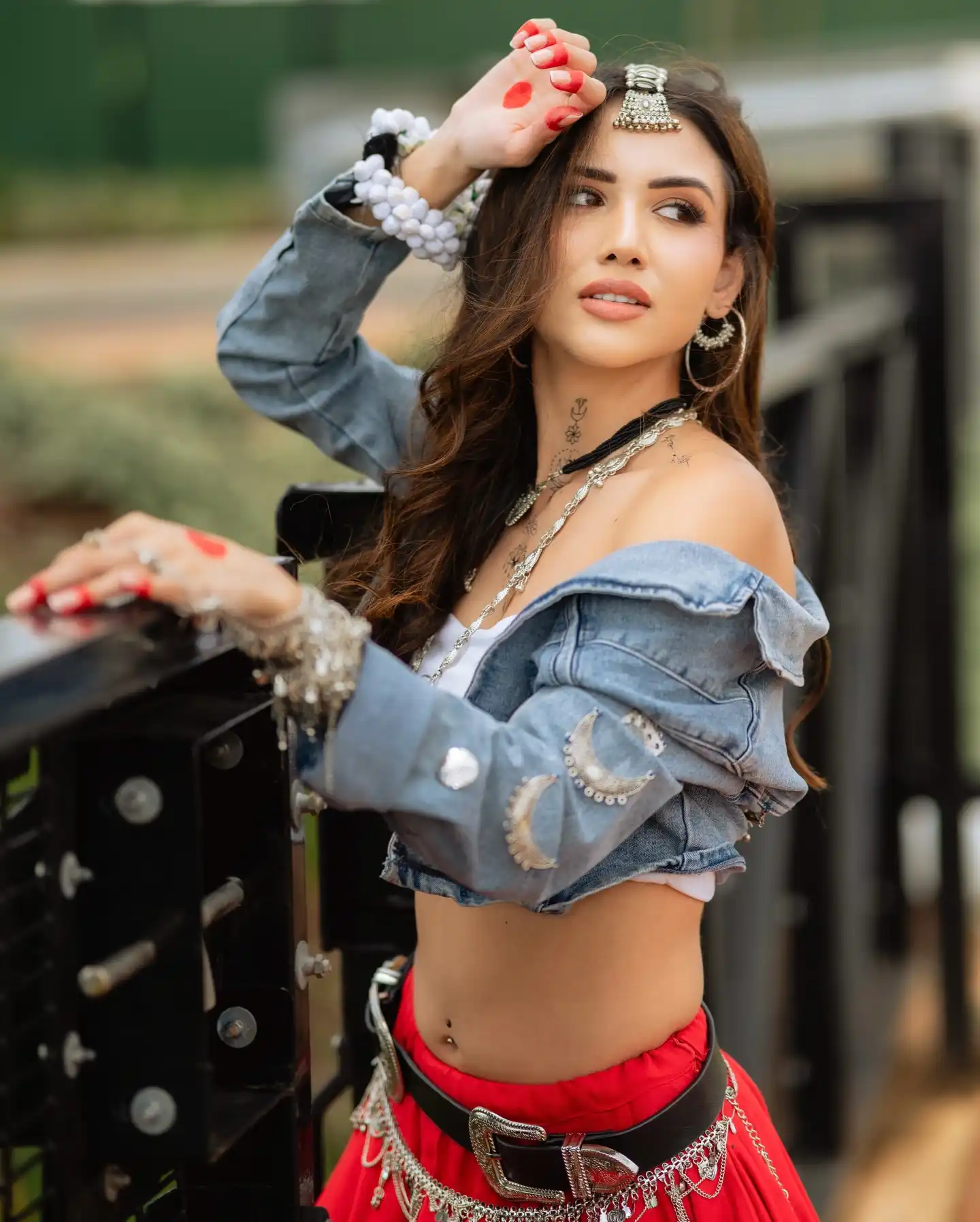 Divaksha Jinabhai looking over her shoulder in a denim jacket, red skirt and silver jewellery, one hand raised to her hair