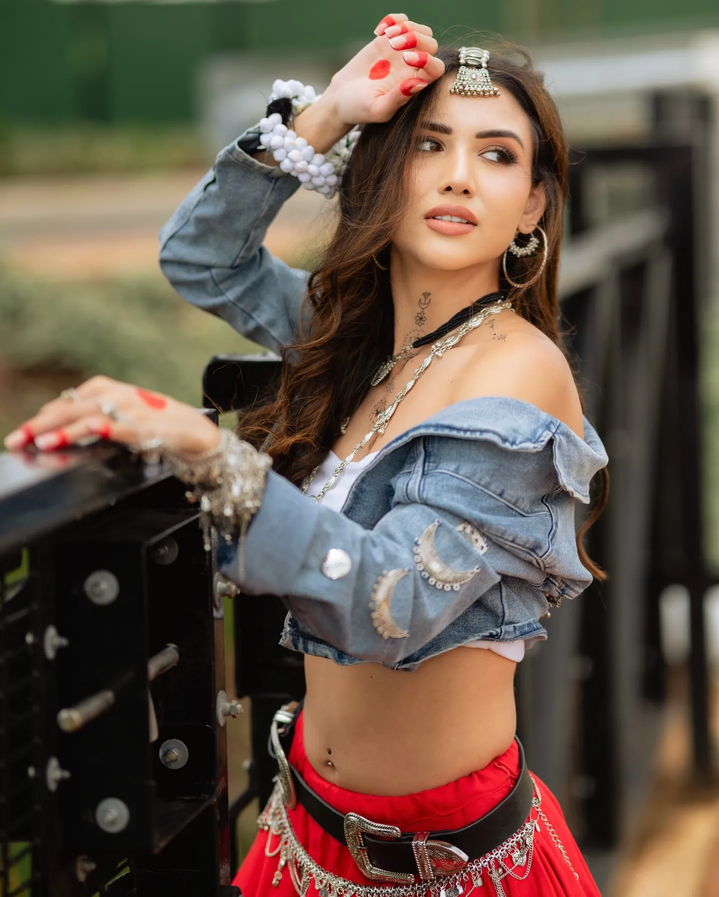 Divaksha Jinabhai looking over her shoulder in a denim jacket and red skirt, leaning on a black railing