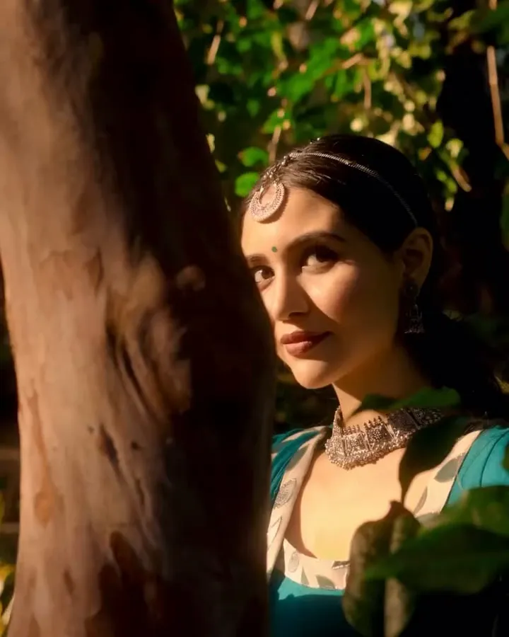 Divaksha Jinabhai looking into the camera from behind a tree, in a still from her Janmashtami film
