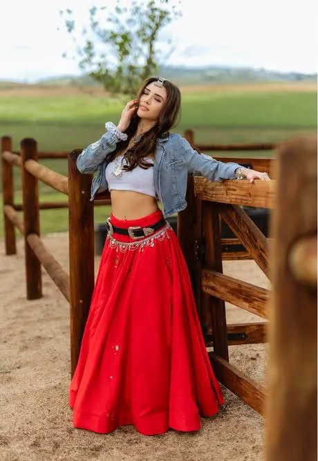 Divaksha Jinabhai in a red lehenga and denim jacket beside a wooden fence