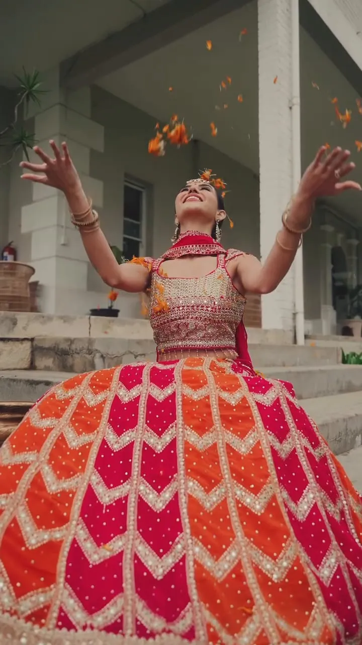 Divaksha Jinabhai in a pink and orange bandhani lehenga, seated beside a brass urli of floating candles and marigold petals