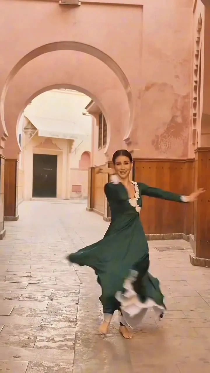 Divaksha Jinabhai in a deep green dress mid-turn under a Moroccan archway